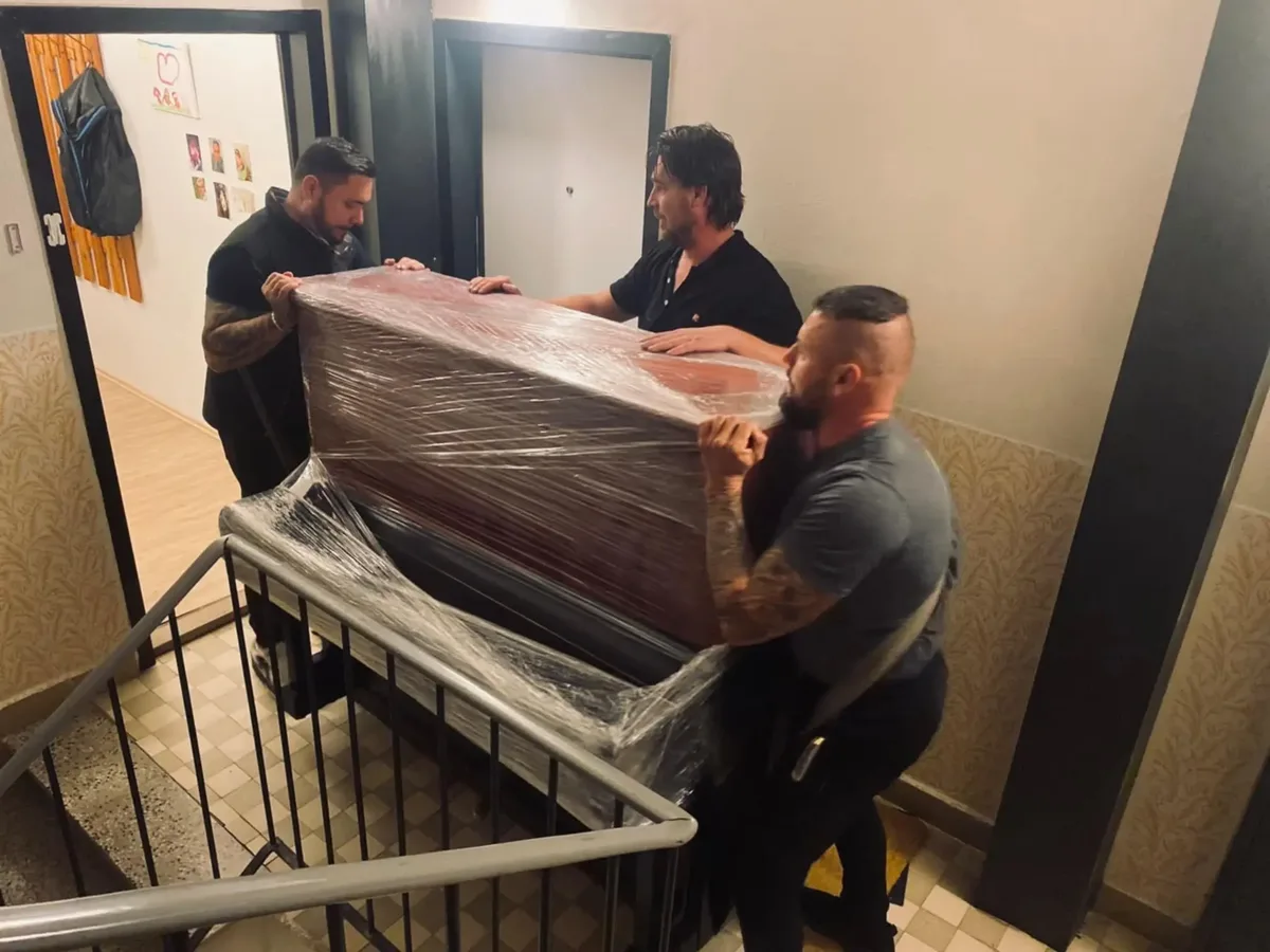 Profesionální stěhováci přenášejí zabalený nábytek po schodech v Brně